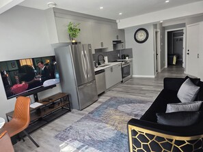 Una cocina moderna con electrodomésticos de acero inoxidable, un comedor con mesa de madera y sillas de cuero, y una sala de estar con sofá negro.