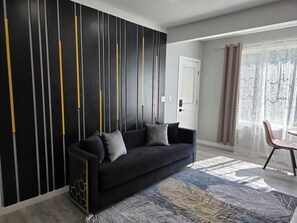 Ein modernes Wohnzimmer mit einem schwarzen Sofa, einem gemusterten Teppich und einer dekorativen Wandverkleidung.