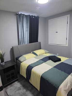 Un dormitorio con una cama, una mesita de noche con una planta, un armario y una ventana con cortinas.