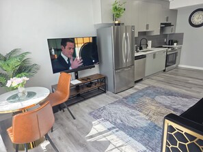 A modern kitchen with a stainless steel refrigerator, a flat-screen TV, and a dining area with a table and chairs. - Bright, Spotless & Spacious Walkout Oasis 15 Minutes from West Edmonton Mall! (Edmonton)