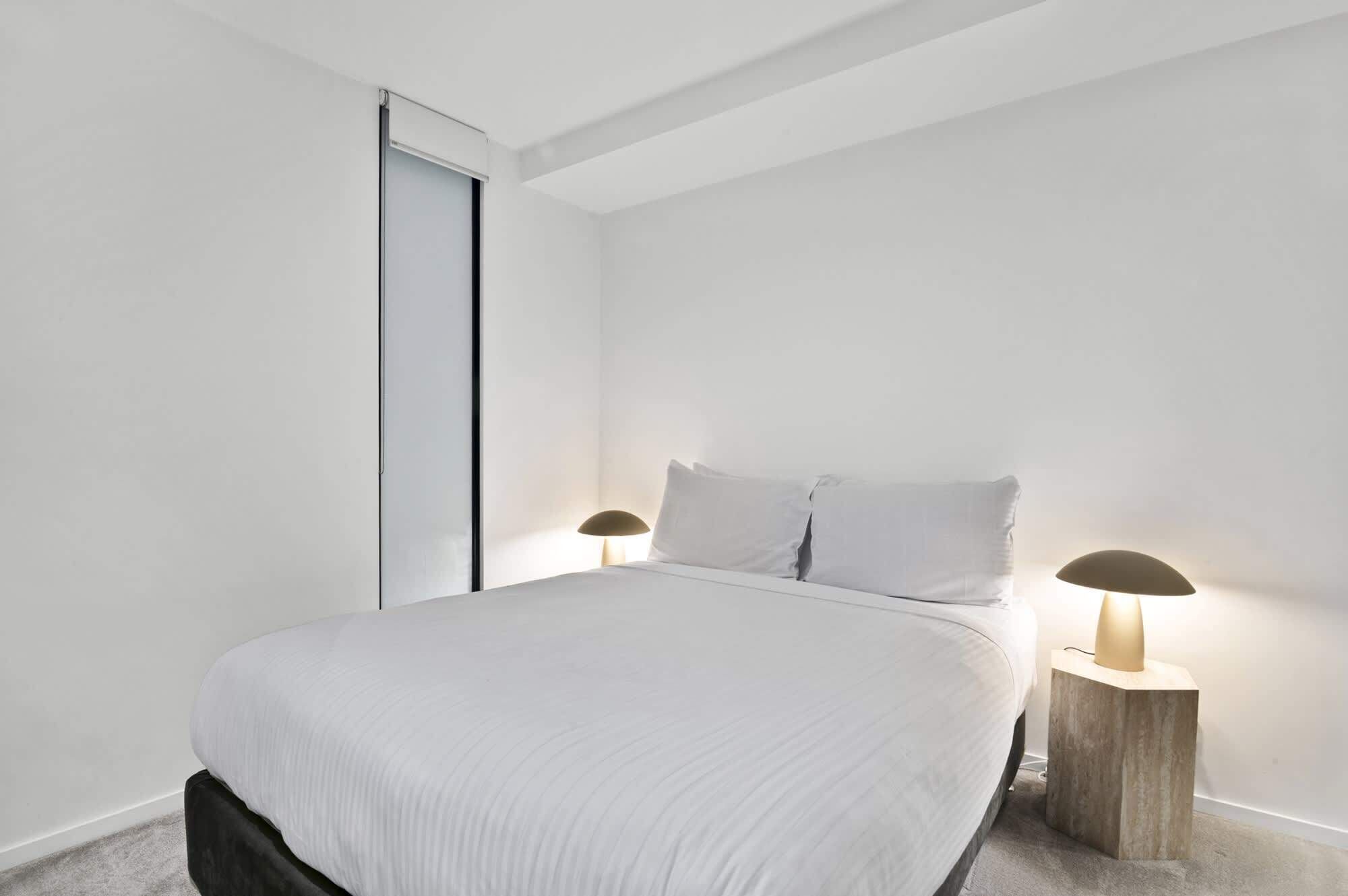 Une chambre à coucher au style minimaliste, avec un lit, deux lampes de chevet et une porte coulissante.