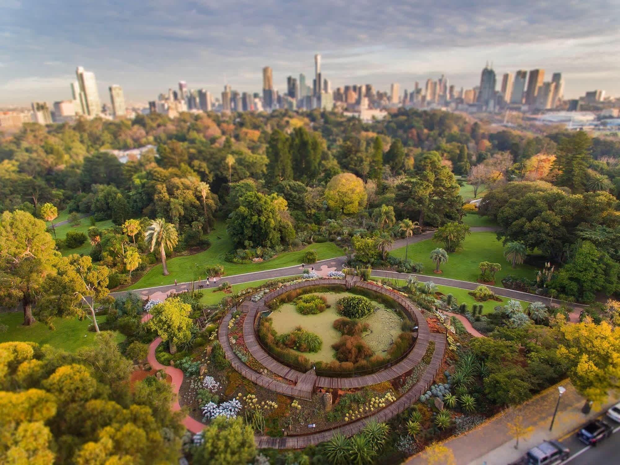 A park with a circular garden, pathways, and a city skyline in the background.