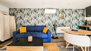 A living room with a blue sofa, a coffee table, and a dining area with a white table and chairs. - Charmante maison avec piscine (Cierzac)
