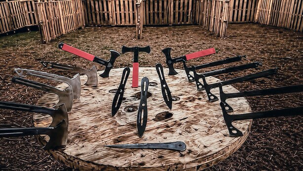 A circular wooden target with various axes and throwing tools arranged around it. - The Whole SquatchVilla: Private 4-Cabin Bigfoot Retreat Near Allegheny NF (Marienville)