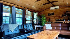 A cabin interior with a wooden ceiling, leather sofas, a wooden table, and a potted plant. - The Whole SquatchVilla: Private 4-Cabin Bigfoot Retreat Near Allegheny NF (Marienville)