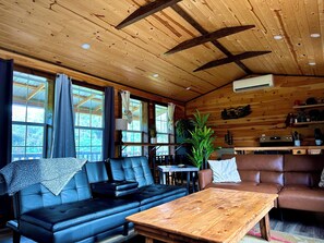 A cabin interior with a wooden ceiling, leather sofas, a wooden table, and a potted plant. - The Whole SquatchVilla: Private 4-Cabin Bigfoot Retreat Near Allegheny NF (Marienville)