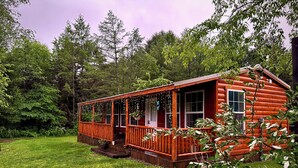 A log cabin with a porch, surrounded by a grassy yard and dense forest. - The Whole SquatchVilla: Private 4-Cabin Bigfoot Retreat Near Allegheny NF (Marienville)
