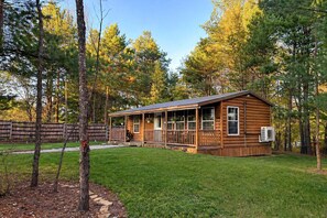 Eine Blockhütte mit Veranda, umgeben von einem grünen Rasen und Bäumen.