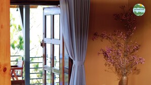 A room with a wooden table, a sofa, a window with curtains, and a vase with flowers.