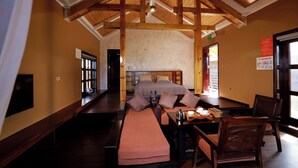 A room with a bed, a bench, a table with a kettle, chairs, and a wooden ceiling.