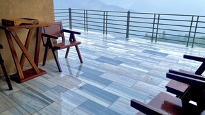 A terrace with a wooden table and chairs, a railing, and a view of distant mountains.