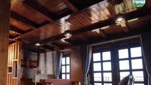 A spacious room with a wooden ceiling, a sofa, a dining table, and large windows.