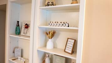 A white shelf with decorative items including a 'WELCOME' sign, a framed quote, and small vases.