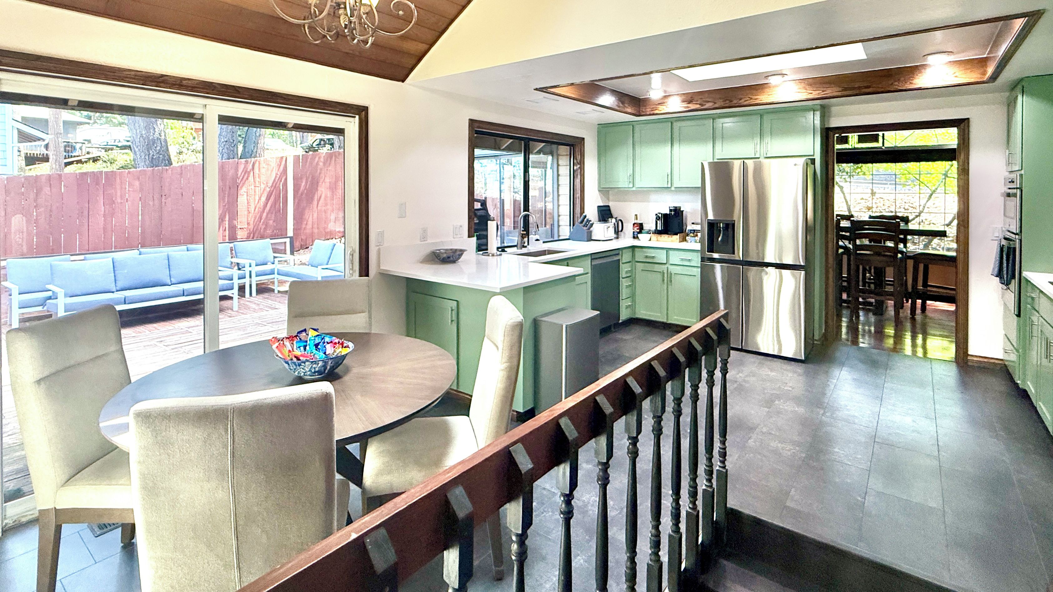 A modern kitchen with green cabinets, a stainless steel refrigerator, and a dining area with a table and chairs.