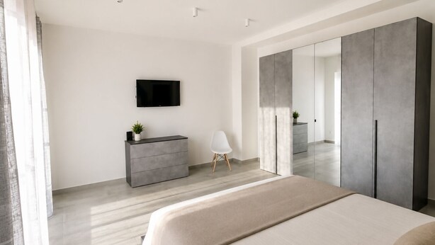 A modern bedroom with a bed, a dresser, a TV, and a wardrobe. - Camera Osanna by Symphonya Rentals (Nardò)