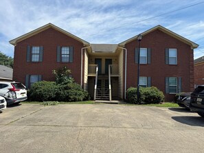 A two-story brick building with a central entrance, a small porch, and a visible staircase leading to the second floor.