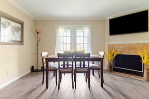 A dining area with a wooden table and chairs, a floor lamp, and a fireplace with yellow flowers.