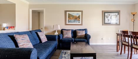 Un salon avec un canapé bleu, une table basse, un tapis et un ventilateur de plafond.