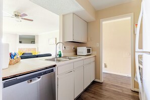 A compact kitchen with a dishwasher, a microwave, and a sink. There is a ceiling fan above the sink and a door leading to another room.