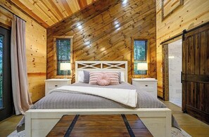 Ein Schlafzimmer mit schrägen Wänden, Holzwänden, einem Bett mit Kopfteil, Nachttischen und Vorhängen.