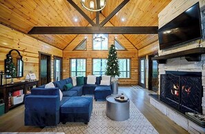 A log cabin interior with a fireplace, a sectional sofa, and a Christmas tree. - Gnarly Ever After | Luxury Meets Fun (Broken Bow)