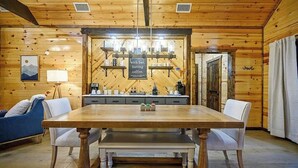 A wooden interior with a dining table, chairs, a bench, a coffee station, and a framed picture on the wall. - Gnarly Ever After | Luxury Meets Fun (Broken Bow)