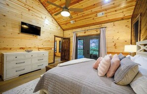 A wooden cabin bedroom with a bed, dresser, TV, and a ceiling fan. - Gnarly Ever After | Luxury Meets Fun (Broken Bow)