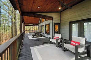 A covered deck with outdoor furniture, a ceiling fan, and a view of the surrounding forest. - Gnarly Ever After | Luxury Meets Fun (Broken Bow)