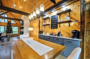 A wooden interior with a kitchen area, a dining table, and a Christmas tree. - Gnarly Ever After | Luxury Meets Fun (Broken Bow)