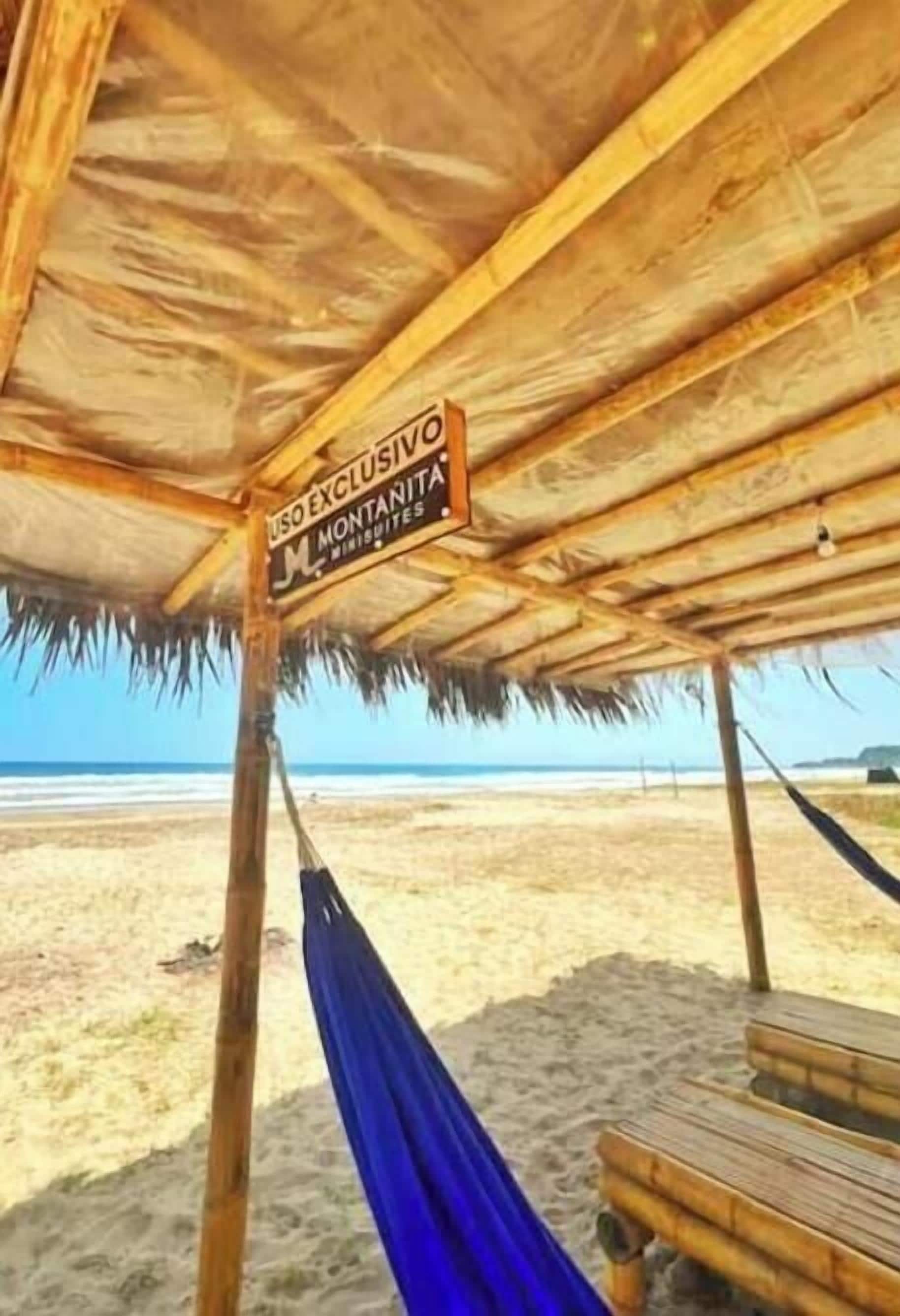 Una cabaña en la playa con techo de paja y una hamaca.