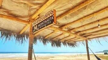 Una cabaña en la playa con techo de paja y una hamaca.