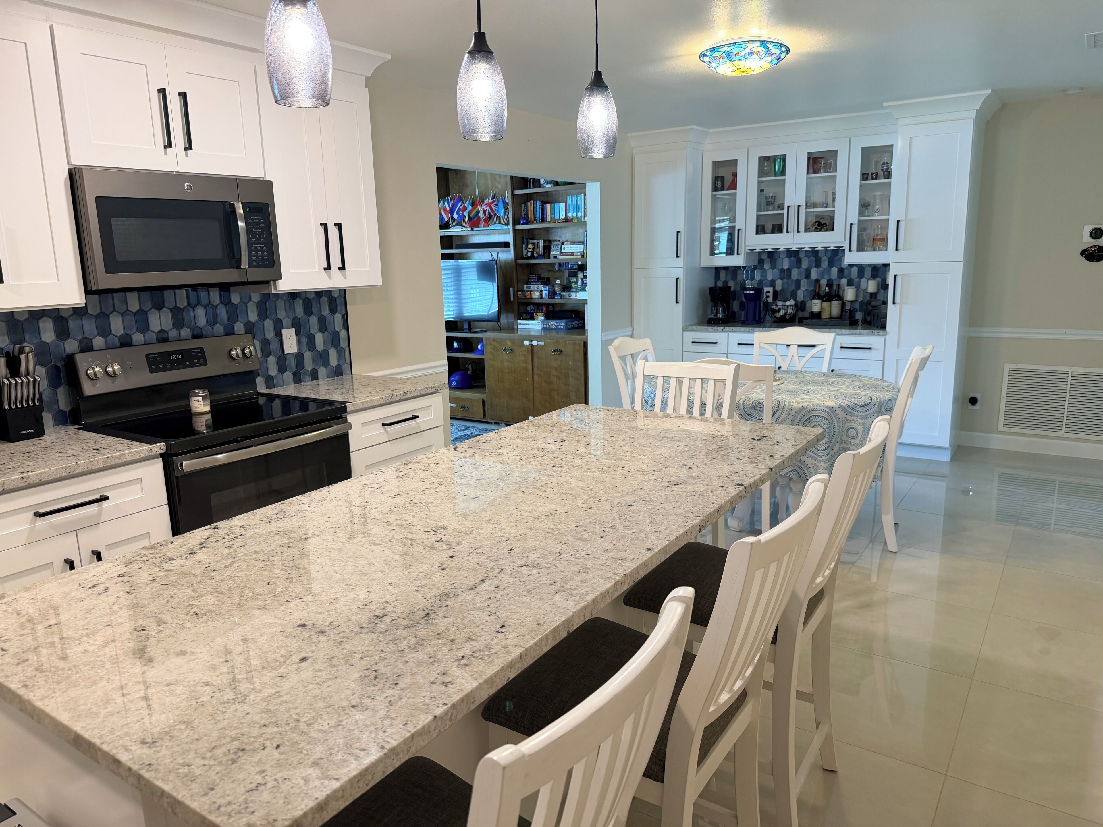 A kitchen with granite countertops, white cabinetry, stainless steel appliances, and pendant lighting.