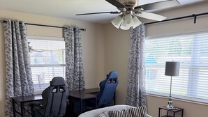 A modern living room with a grey sofa, a gaming chair, a desk, and a ceiling fan. - Family-Friendly 2-bedroom 2-bath house close to Tampa Airport (Tampa)