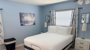 A bedroom with a bed, nightstands, a lamp, a trash bin, and a painting on the wall. - Family-Friendly 2-bedroom 2-bath house close to Tampa Airport (Tampa)