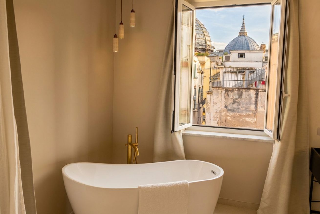 A bathroom with a freestanding bathtub, a window with a view of buildings, and a curtain.