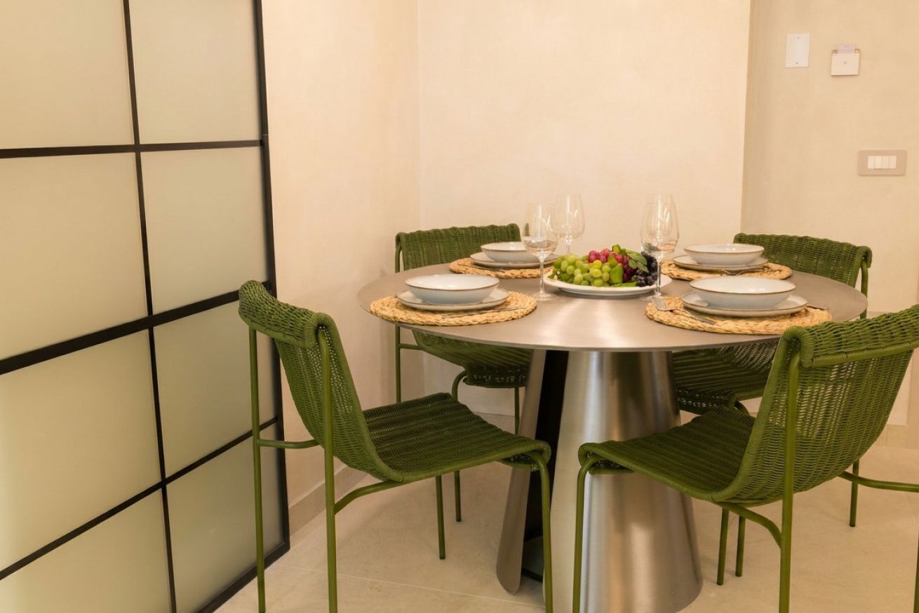 A round dining table with four chairs, a fruit bowl, and wine glasses.