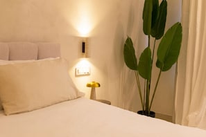 Ein Bett mit weißer Bettwäsche, eine Nachttischlampe, eine Wandleuchte und ein Topfpflanze.