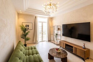 Ein modernes Wohnzimmer mit einem grünen Sofa, einem runden Couchtisch, einem Fernseher und einer Pendelleuchte.