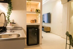 Eine moderne Küche mit Einbaukühlschrank, Spüle und Arbeitsplatte mit Kaffeemaschine. Regale mit Dekoration und eine hängende Pflanze sind ebenfalls vorhanden.