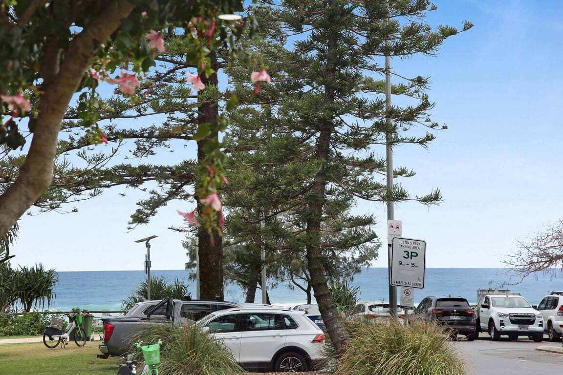 A parking area with cars, a sign indicating 3P parking, and a view of the ocean.