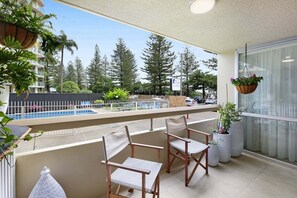 Ein Balkon mit zwei Stühlen, Blumentöpfen und Blick auf ein Schwimmbecken und Bäume.