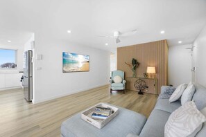 Un salon moderne comprenant un canapé, un fauteuil, une table avec des magazines, un tableau, un ventilateur de plafond et un mur recouvert de panneaux en bois.