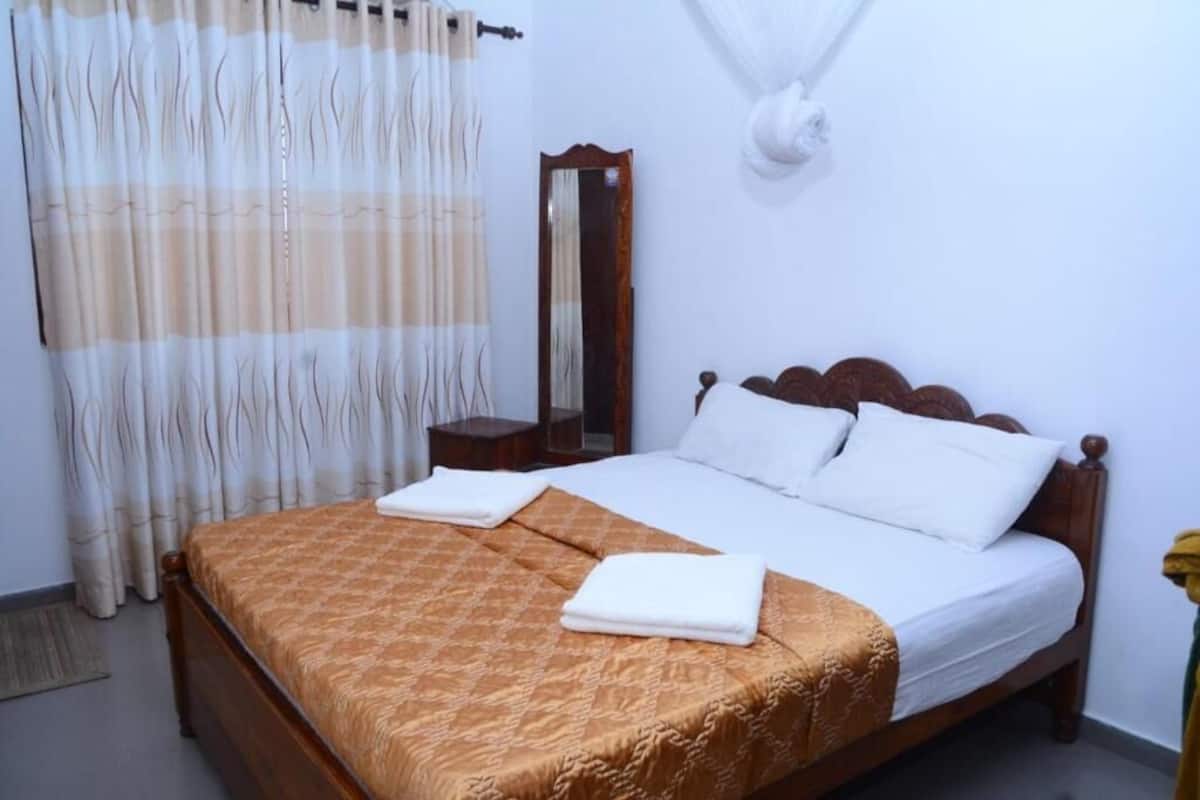 A neatly made bed with a patterned bedspread, a bedside table with a lamp, and a mirror on the wall.