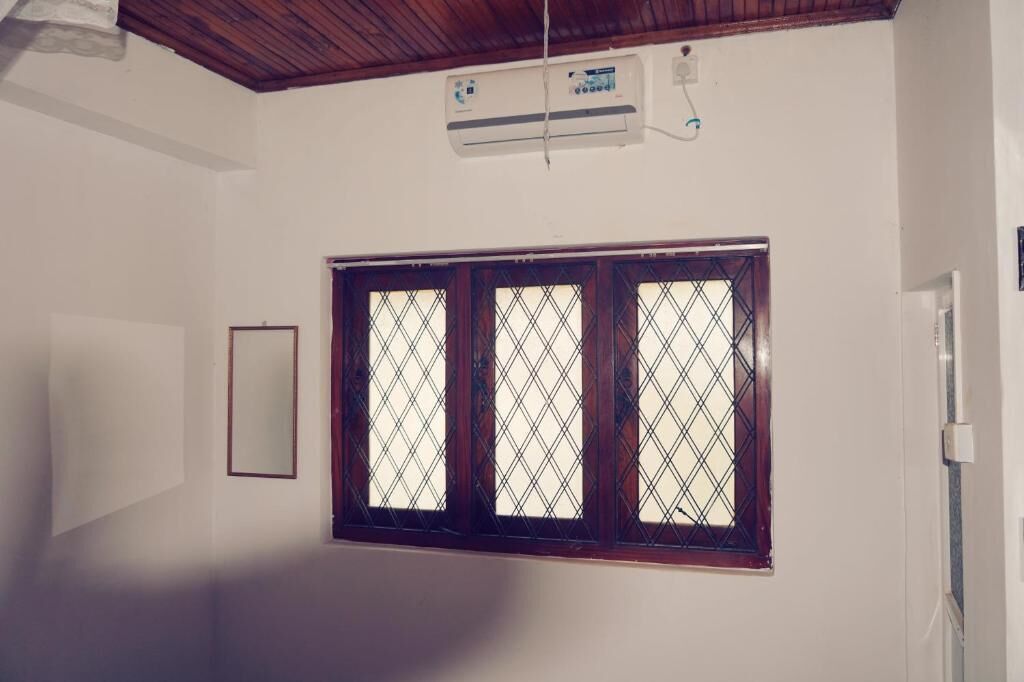 Una habitación con techo de madera, un equipo de aire acondicionado, una ventana con marco de madera y una puerta.