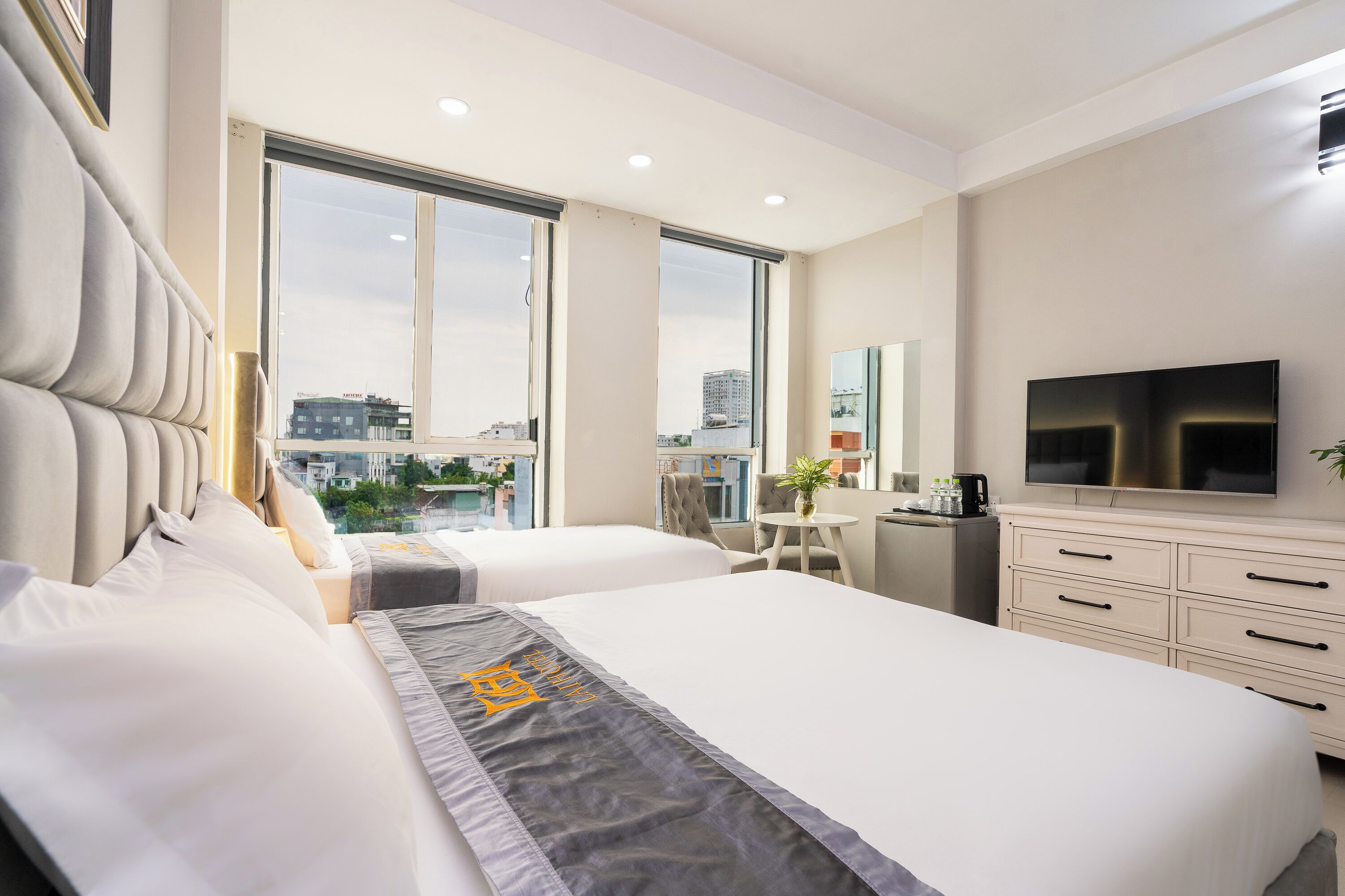 Habitación de hotel moderna con dos camas, televisión, escritorio y un amplio ventanal con vista a la ciudad.
