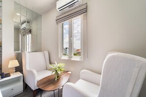 A modern room with two white armchairs, a small wooden table with a plant, a mirror, and an air conditioning unit. - Lai Hotel Phu Nhuan - Near Tan Dinh Church & District 1 (Ho Chi Minh City)