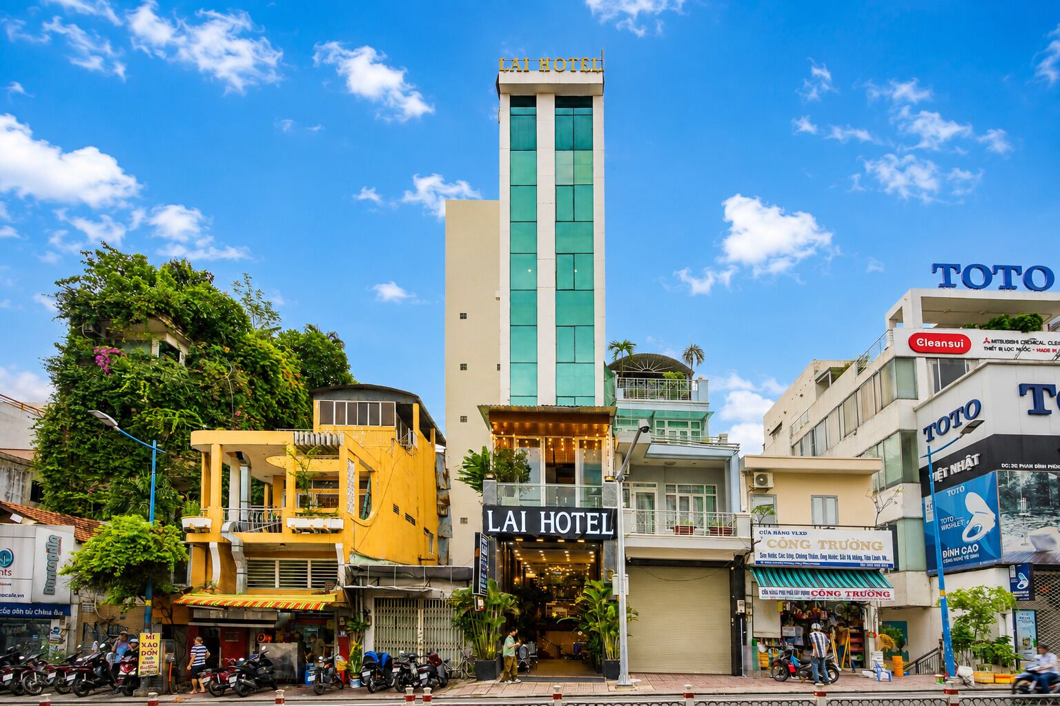 Un hotel con un cartello ben visibile, un edificio alto dalla facciata verde e un negozio TOTO.