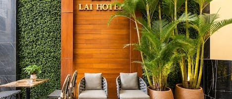 A hotel reception area with a wooden wall, two chairs, a table, and a potted plant.