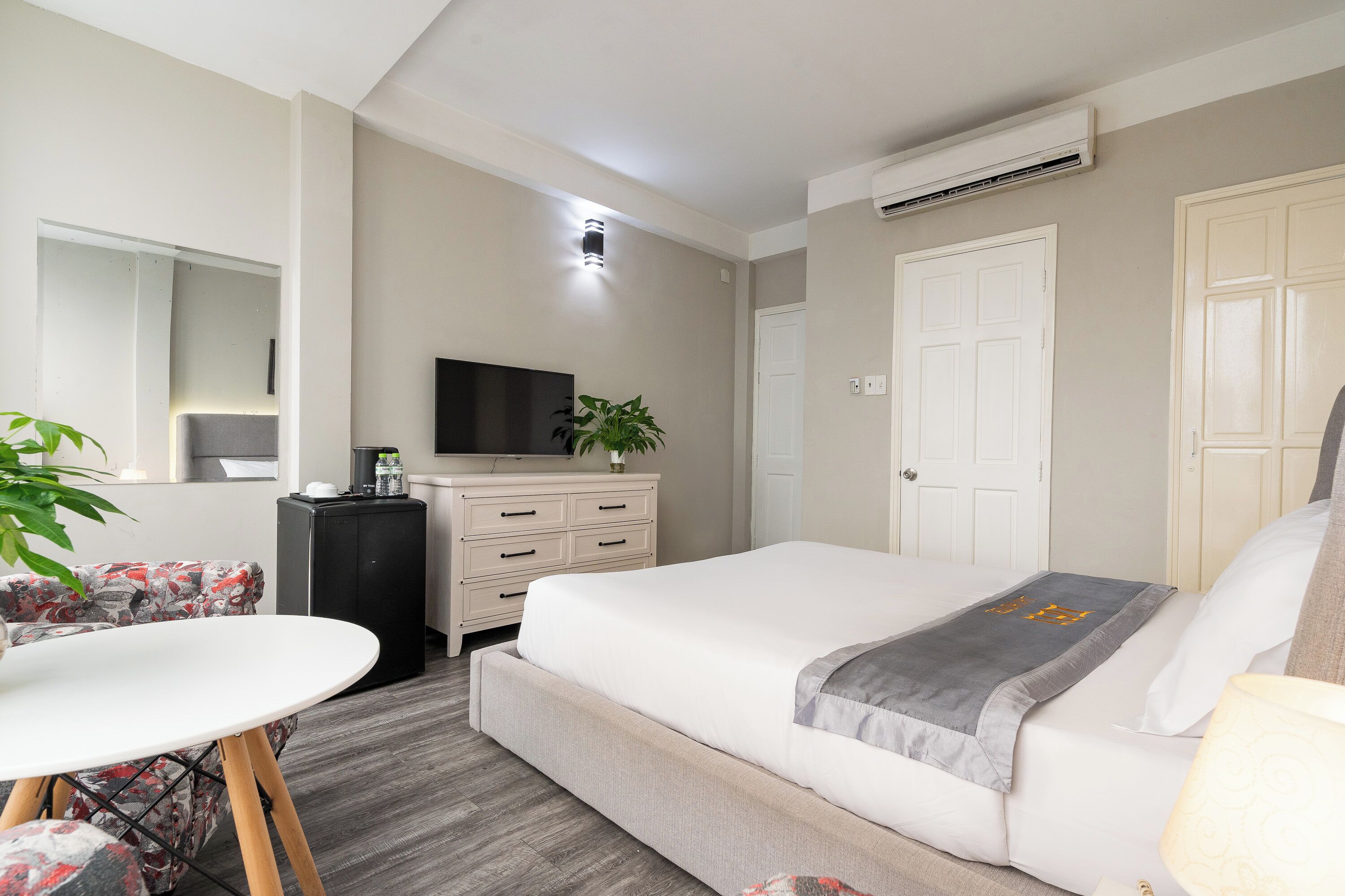 Ein Hotelzimmer mit Bett, Schreibtisch, Stuhl, Kommode, Fernseher und einer Zimmerpflanze.
