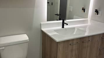 A bathroom with a white toilet, wooden cabinets, a white sink, and a mirror.